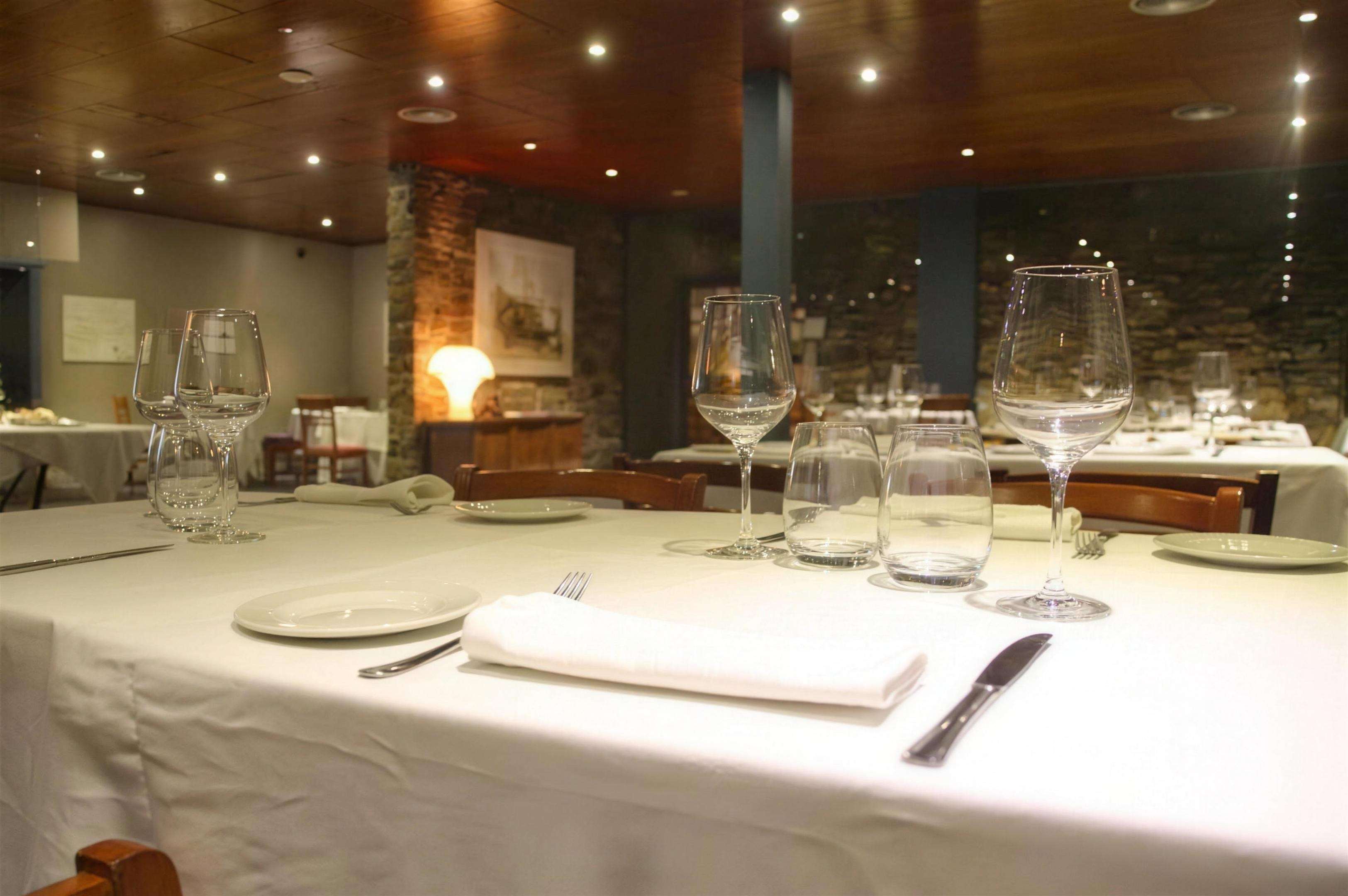 A laid table in the foreground, the lit dining room and its wooden ceiling behind.